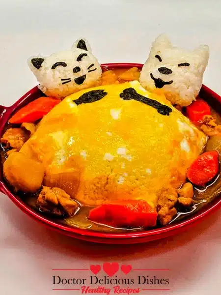 Finished dish: chicken curry with potatoes and carrots, topped with a fluffy omelet and garnished with rice shaped like cat faces, a whimsical presentation of a Japanese Chicken Curry Recipe.
