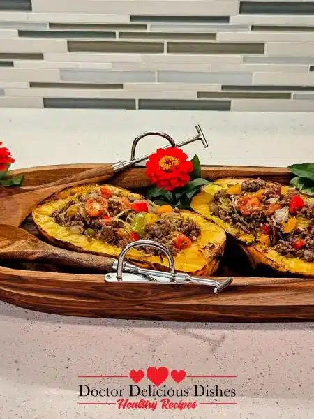 Beautifully plated ground beef recipe with spaghetti squash served inside the grilled squash shells in a wooden serving tray with flowers for decoration.