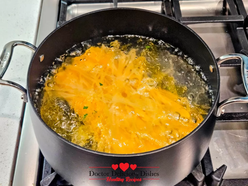 Long pasta noodles actively boiling in a pot of water with oil for a Chicken Alfredo Recipe with Jar Sauce.