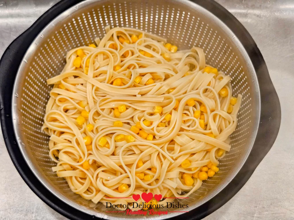 Freshly cooked pasta and corn in a colander, ready to be combined with Alfredo sauce and chicken for a Chicken Alfredo Recipe with Jar Sauce.