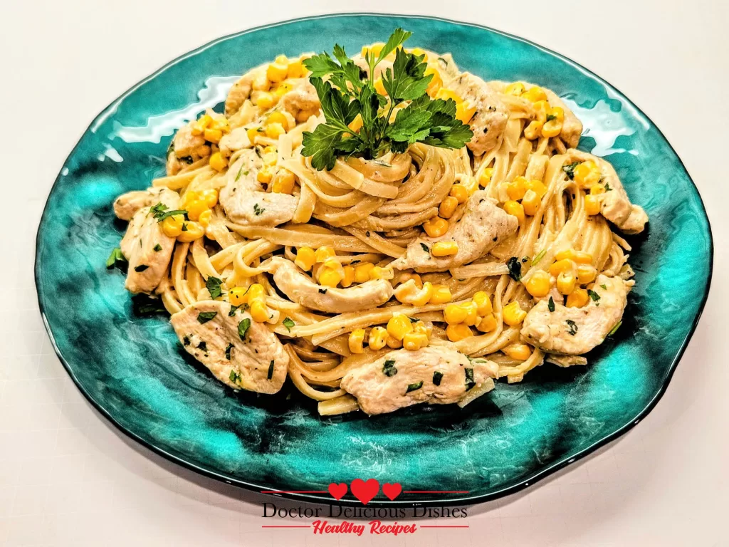 A completed plate of Chicken Alfredo pasta with corn, garnished with fresh parsley and served on a turquoise dish for a Chicken Alfredo Recipe with Jar Sauce.