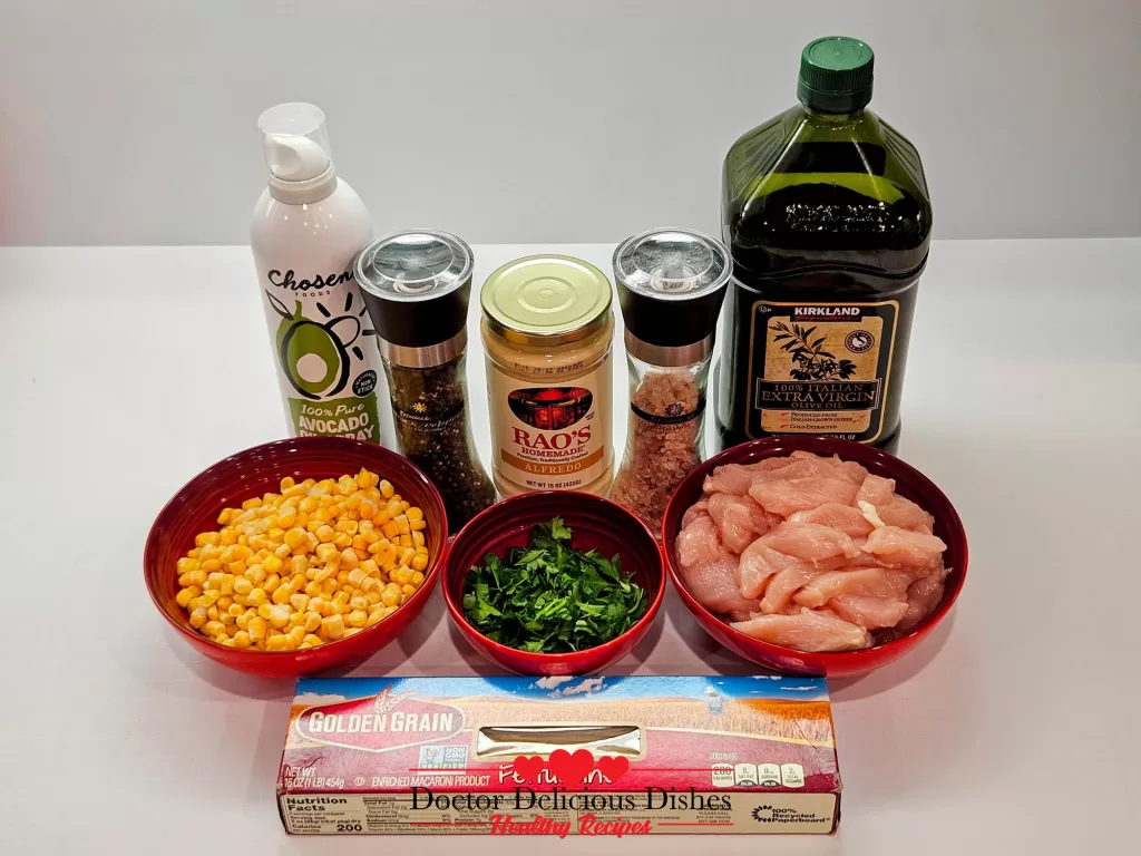 All the ingredients for a Chicken Alfredo Recipe with Jar Sauce displayed on a counter, including pasta, raw chicken, corn, cilantro, alfredo sauce, cooking oils, and seasonings.