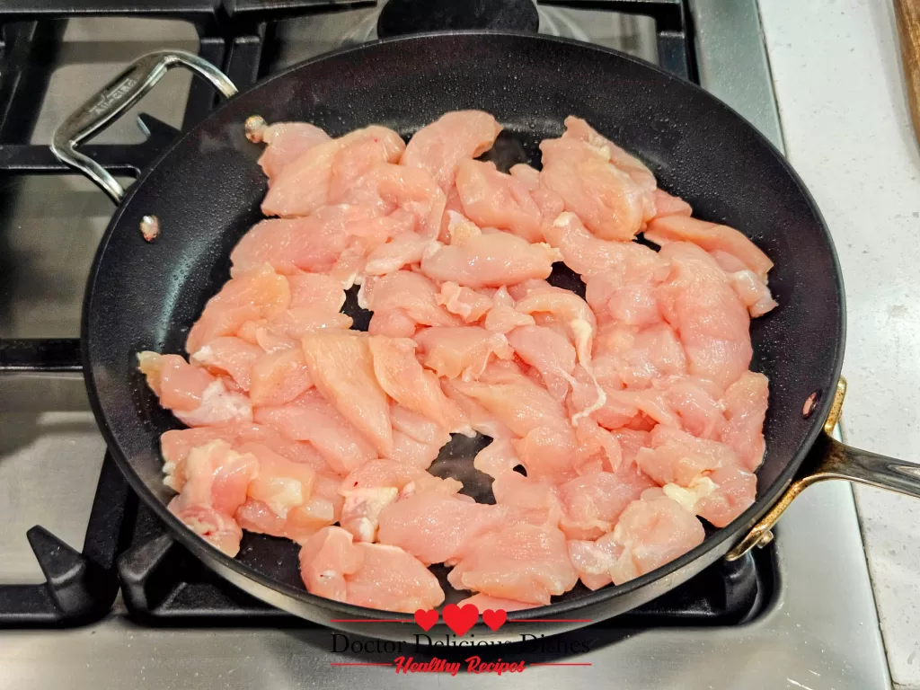 Strips of raw chicken placed in a nonstick pan, about to be cooked for a Chicken Alfredo Recipe with Jar Sauce.