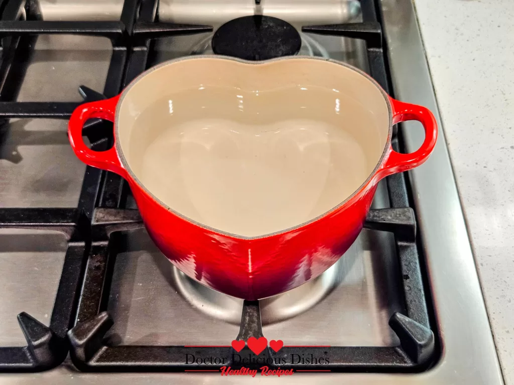 A red heart-shaped Le Creuset pot filled with water, preparing for Easy Tong Sui Recipe on a stovetop.