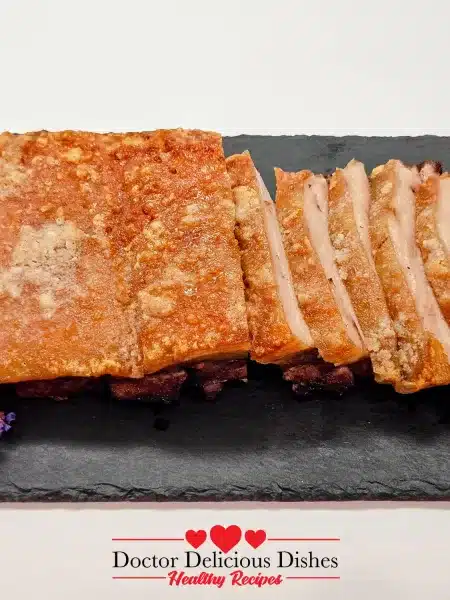 Golden, crispy pork belly sliced and served on a black slate platter, garnished with edible flowers.