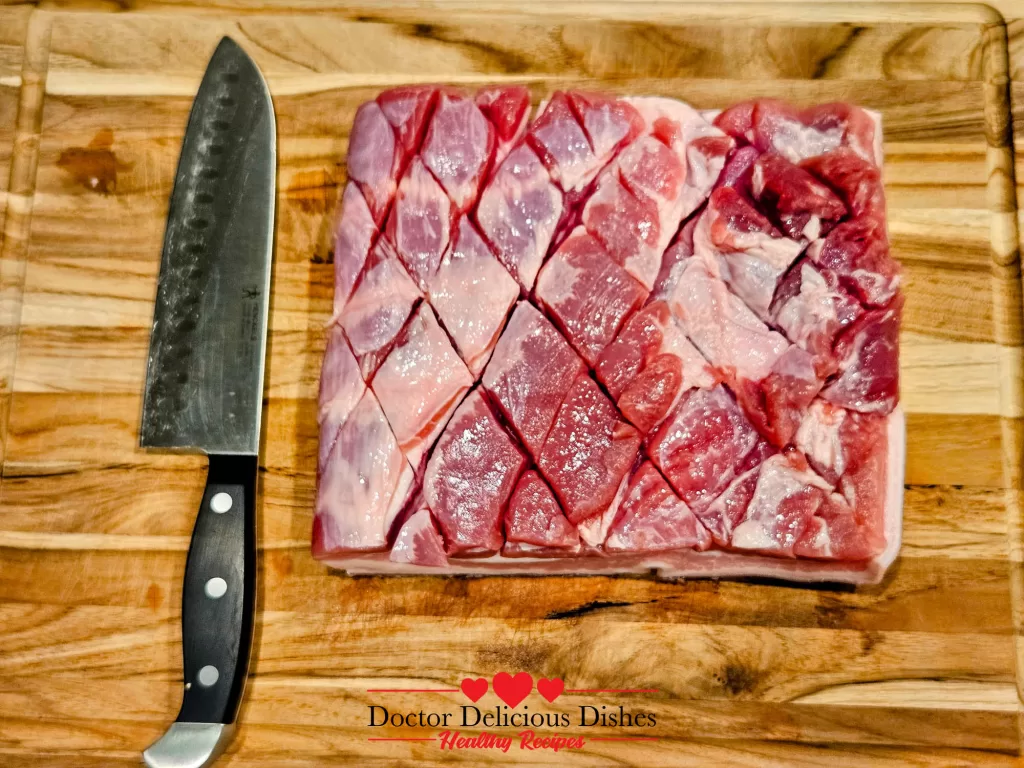 Pork belly scored in a diamond pattern on a wooden cutting board, ready for seasoning and cooking.