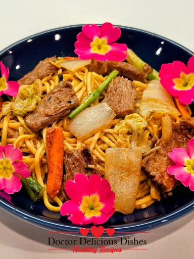 Plated Beef Lo Mein in a dark blue dish, topped with edible flowers for a vibrant presentation