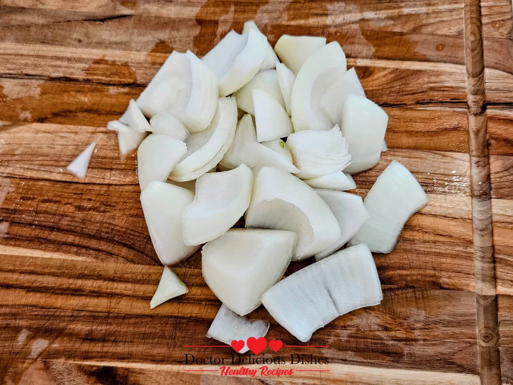 Roughly chopped yellow onion pieces on a wooden cutting board