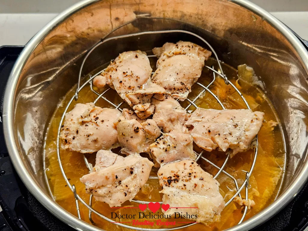 Cooked chicken thighs resting on trivet inside the Instant Pot with broth below