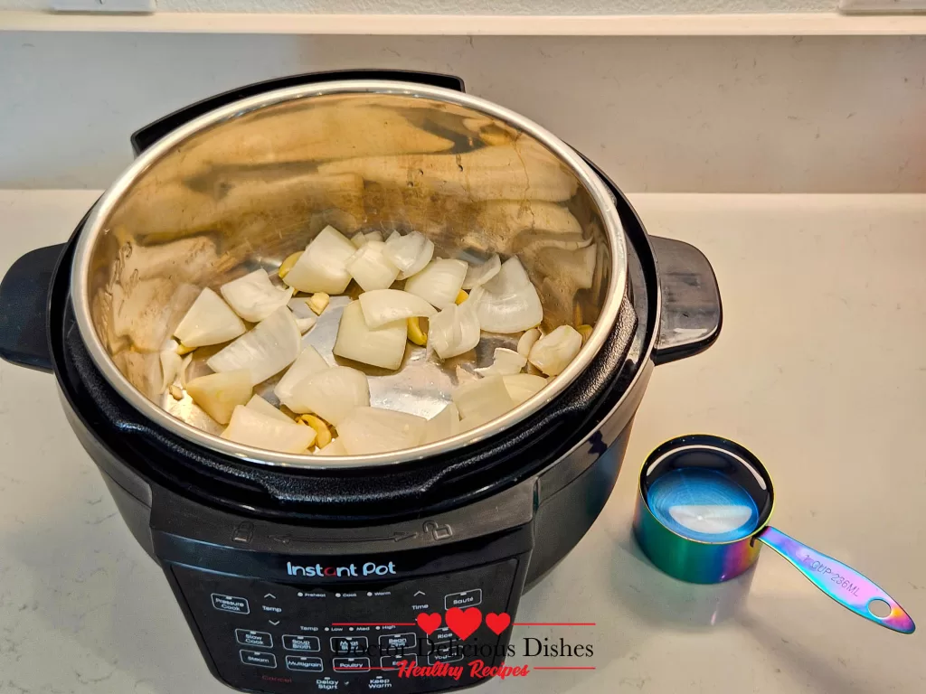 Chopped onions and garlic inside an Instant Pot with a measuring cup of water