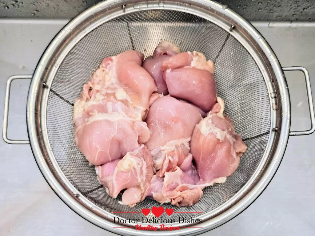 Raw boneless skinless chicken thighs in a colander being rinsed before cooking
