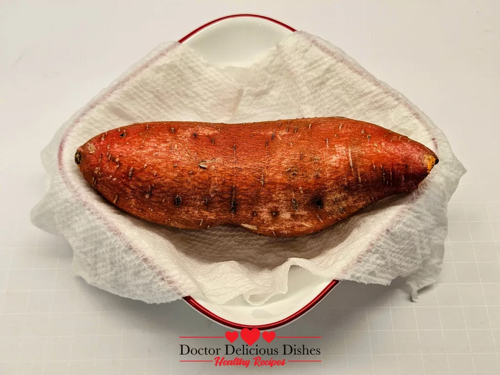 A whole sweet potato placed in a dish lined with a damp paper towel, ready for microwaving
