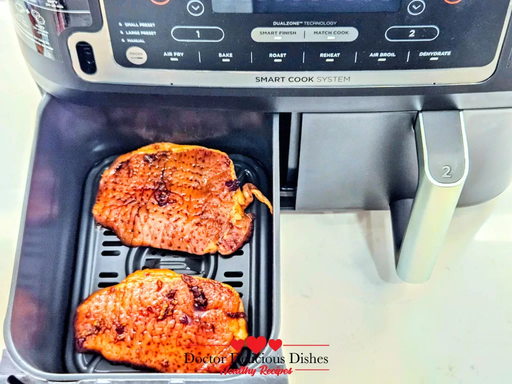 Two boneless thin cut air fryer pork chops in one zone of a dual-zone air fryer, showing the air fryer's digital display, ready to cook.