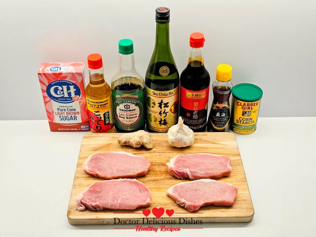 All ingredients for air fryer boneless thin cut pork chops laid out, including four raw boneless pork chops on a cutting board, soy sauce, mirin, sugar, garlic, ginger, and cornstarch.