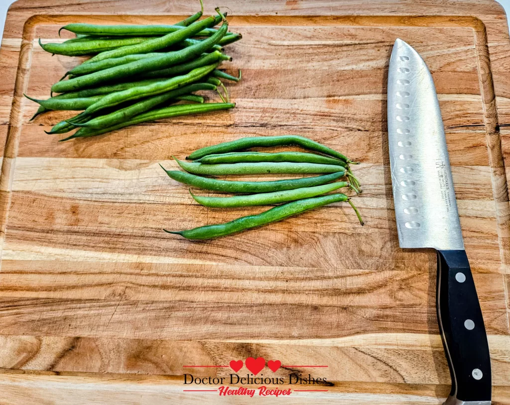 Trimming the ends of fresh green beans on a cutting board with a chef’s knife for Air Fryer Green Beans
