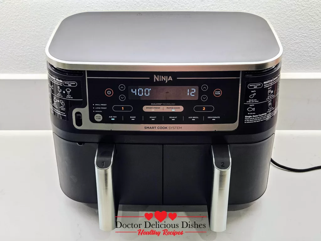 Dual air fryer setup with Air Fryer Chicken Thighs on one side and seasoned potato wedges on the other.