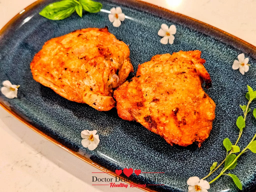 Close-up of two perfectly crispy Air Fryer Chicken Thighs on a floral blue plate, garnished with herbs.