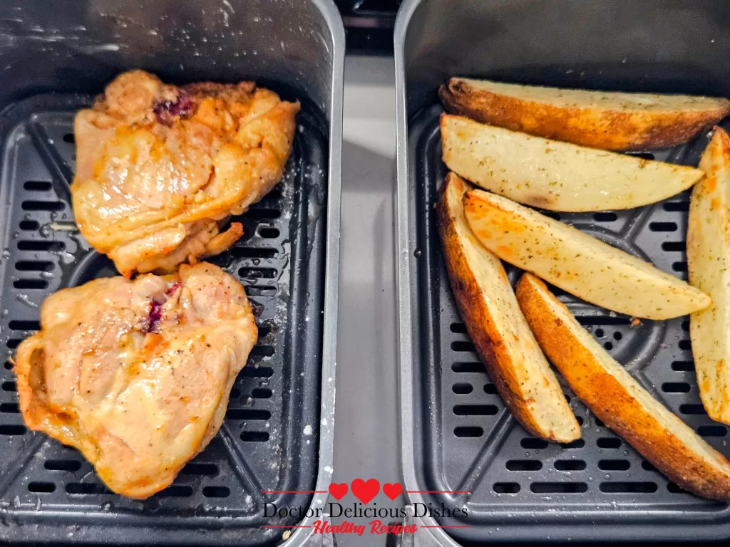 Air Fryer Chicken Thighs flipped and fully cooked with golden crispy skin alongside browned potato wedges.