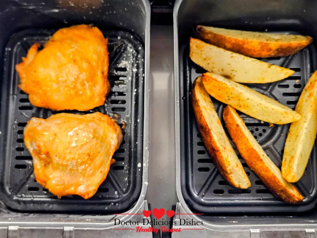 Air Fryer Chicken Thighs and potato wedges halfway through cooking, showing golden crisp edges.