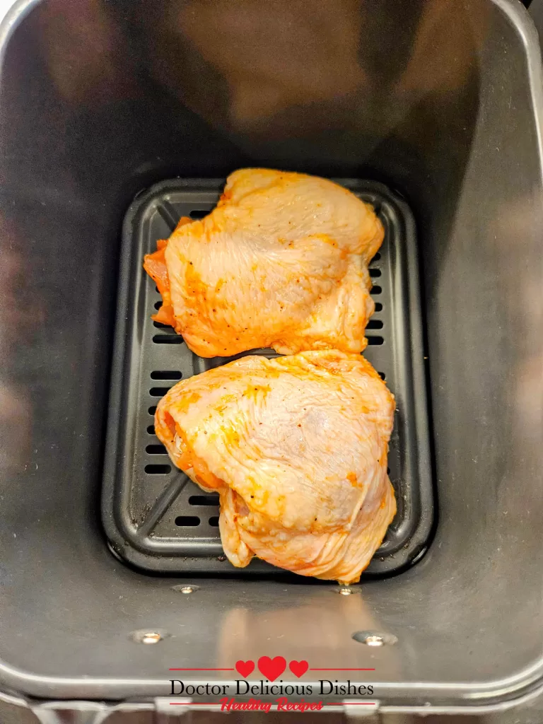 Raw, seasoned chicken thighs placed skin-side up in the air fryer basket for Air Fryer Chicken Thighs.