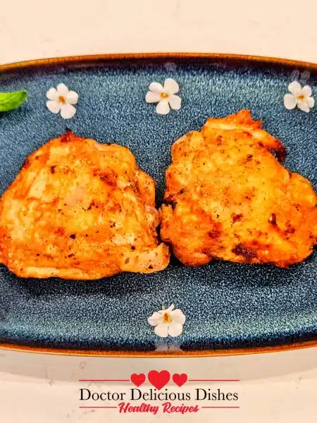 Final plated Air Fryer Chicken Thighs on a blue flower dish, garnished with fresh herbs.