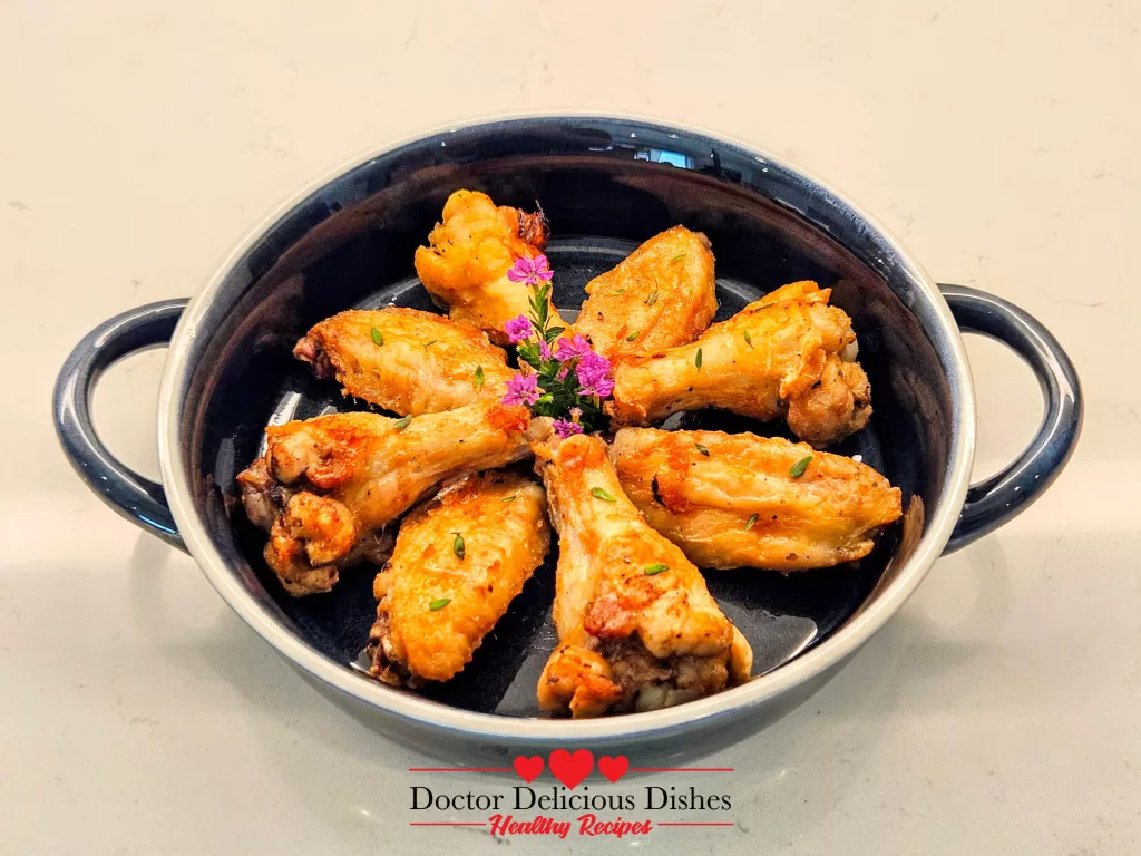 Cooked air fryer chicken wings plated and garnished with herbs and purple edible flowers.