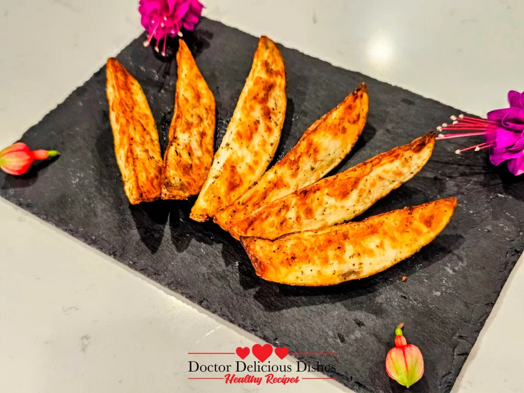 Crispy Air Fryer Potato Wedges plated on a slate board, fanned out next to decorative flowers.