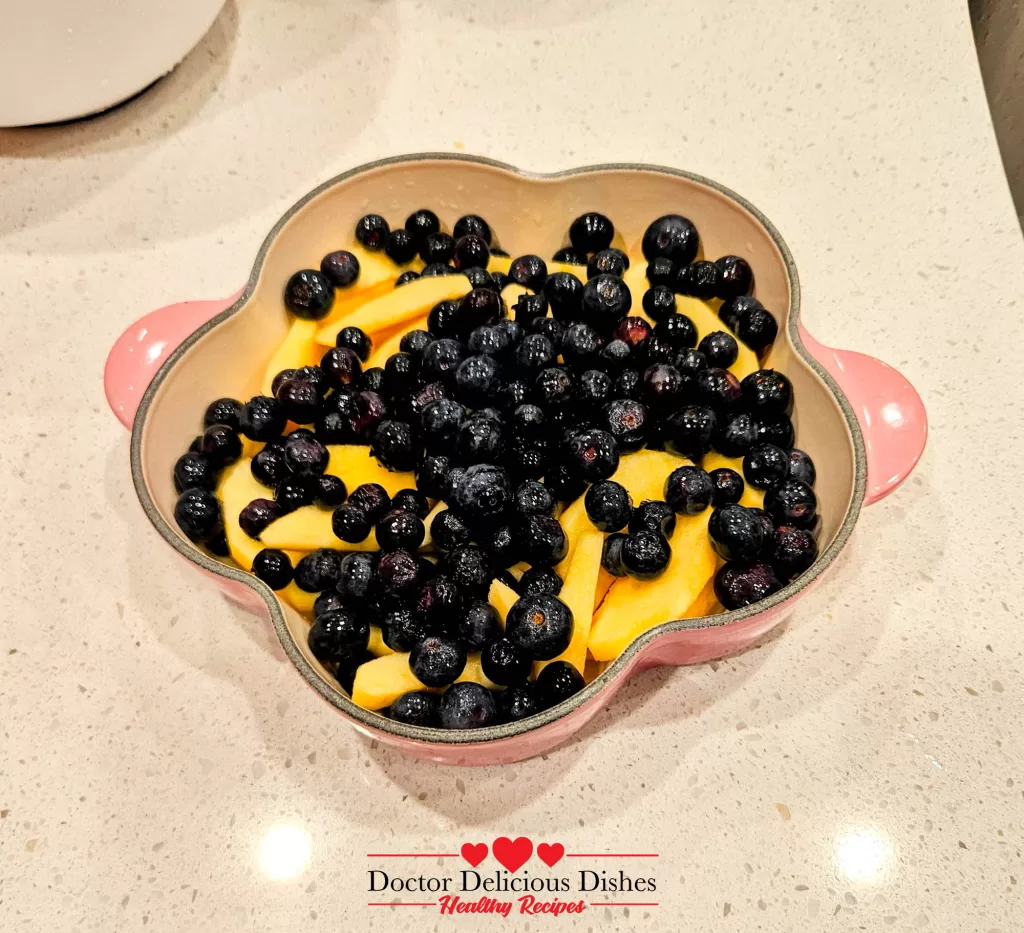 Apples and blueberries layered in a pink baking dish for apple blueberry crumble recipe.