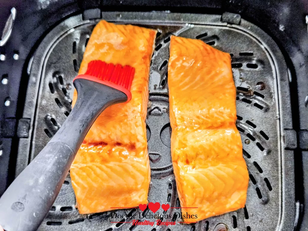 Brushing teriyaki glaze onto salmon in the air fryer for glossy Teriyaki Salmon.