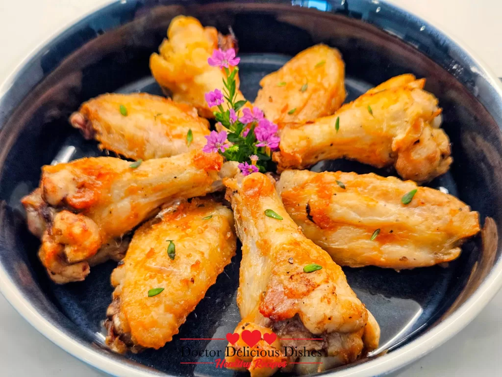 Close-up shot of golden brown air fryer chicken wings garnished with thyme and edible flowers.