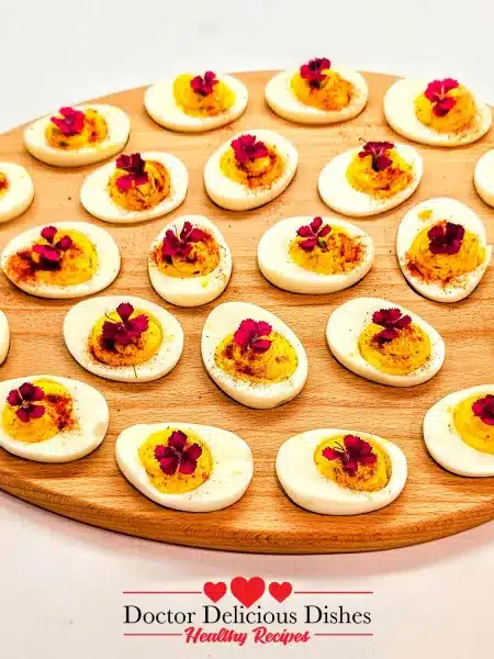 Deviled Eggs Recipe – finished platter of deviled eggs garnished with paprika and herbs on wooden board