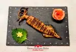 Japanese grilled squid (Ikayaki) beautifully plated on black slate with decorative rose shaped pink pickled ginger garnish and shiso leaf with Kewpie Star.