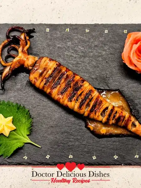 Japanese grilled squid (Ikayaki) beautifully plated on black slate with decorative rose shaped pink pickled ginger garnish and shiso leaf with Kewpie Star.