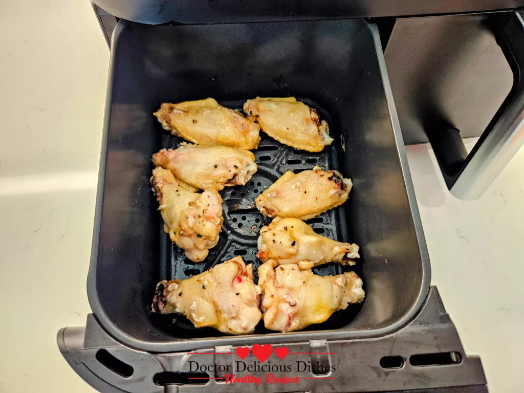 Lightly golden chicken wings halfway through cooking time inside the air fryer basket.