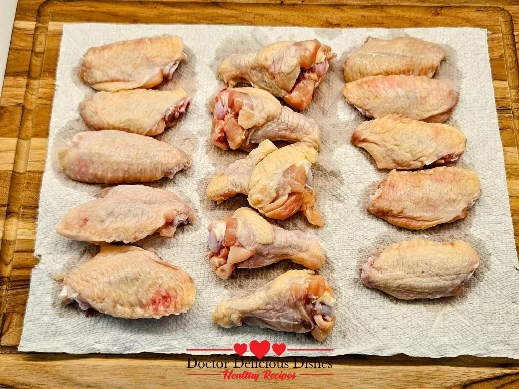 Raw chicken wings patted dry with paper towels on a wooden cutting board before air frying.
