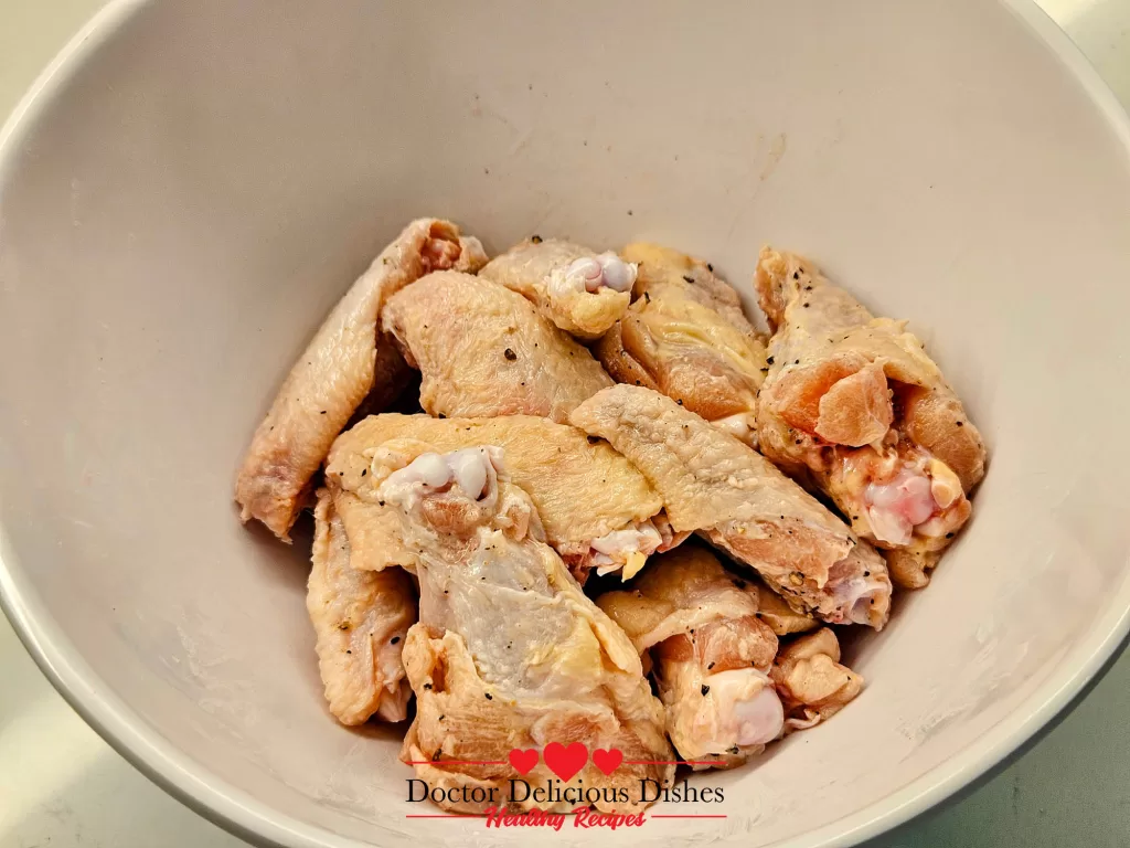 Chicken wings seasoned with cornstarch, baking powder, salt, and pepper in a white bowl.