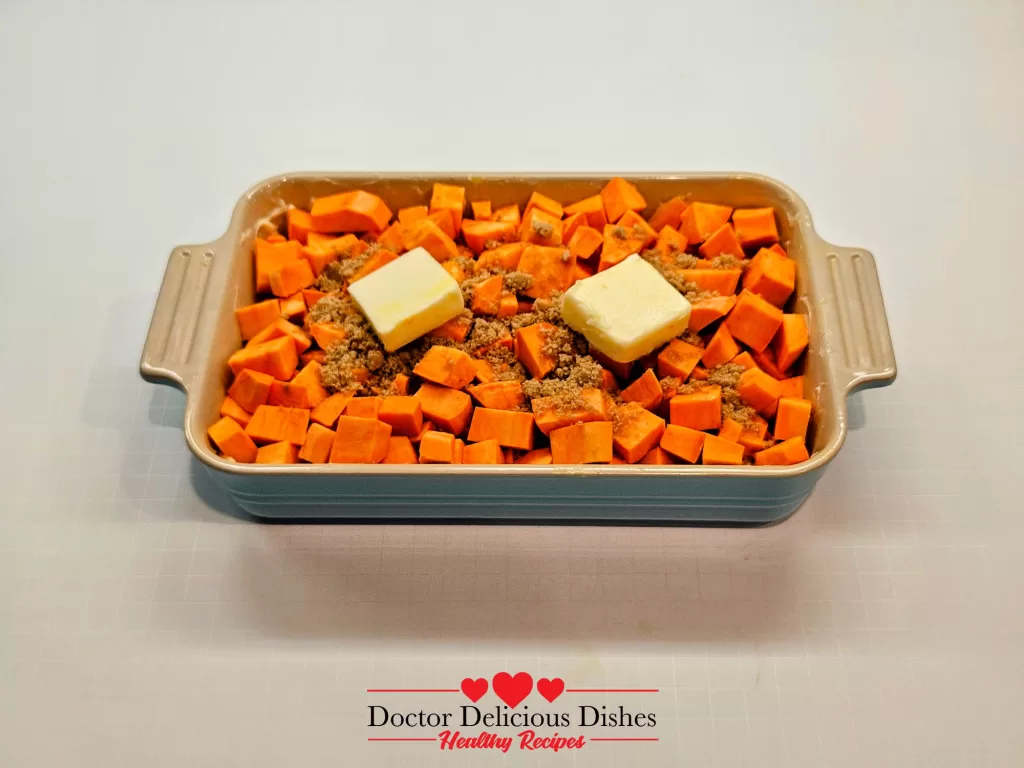 Cubed sweet potatoes layered with brown sugar and butter in a baking dish for sweet potato casserole recipe.