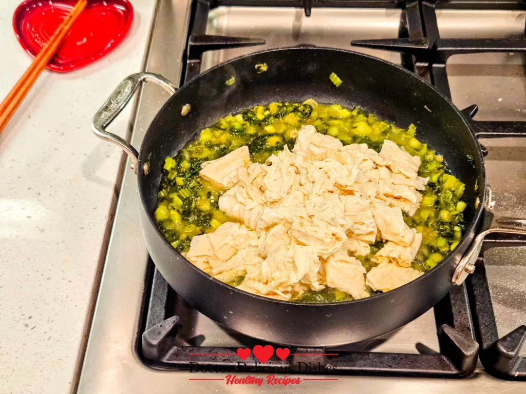Softened tofu skin added to sautéed preserved mustard greens in pan for tofu skin recipe.