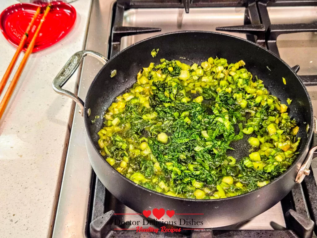 Preserved mustard greens sautéing in skillet with broth for tofu skin recipe.