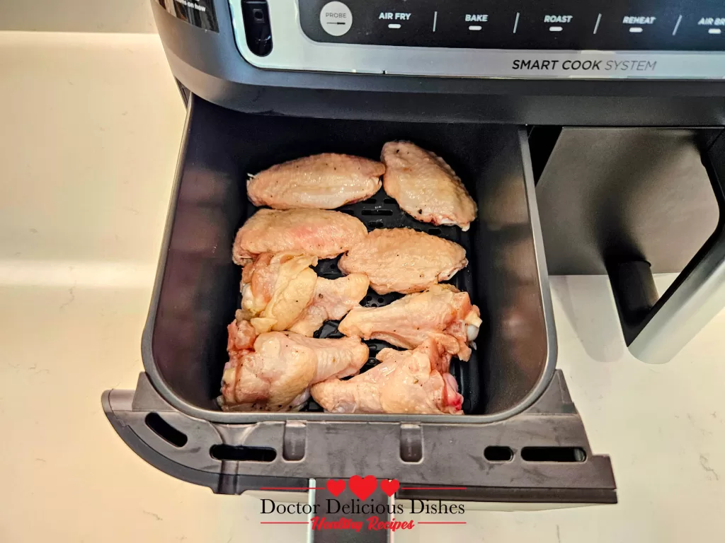 Raw seasoned chicken wings arranged in a single layer in the air fryer basket ready to cook.