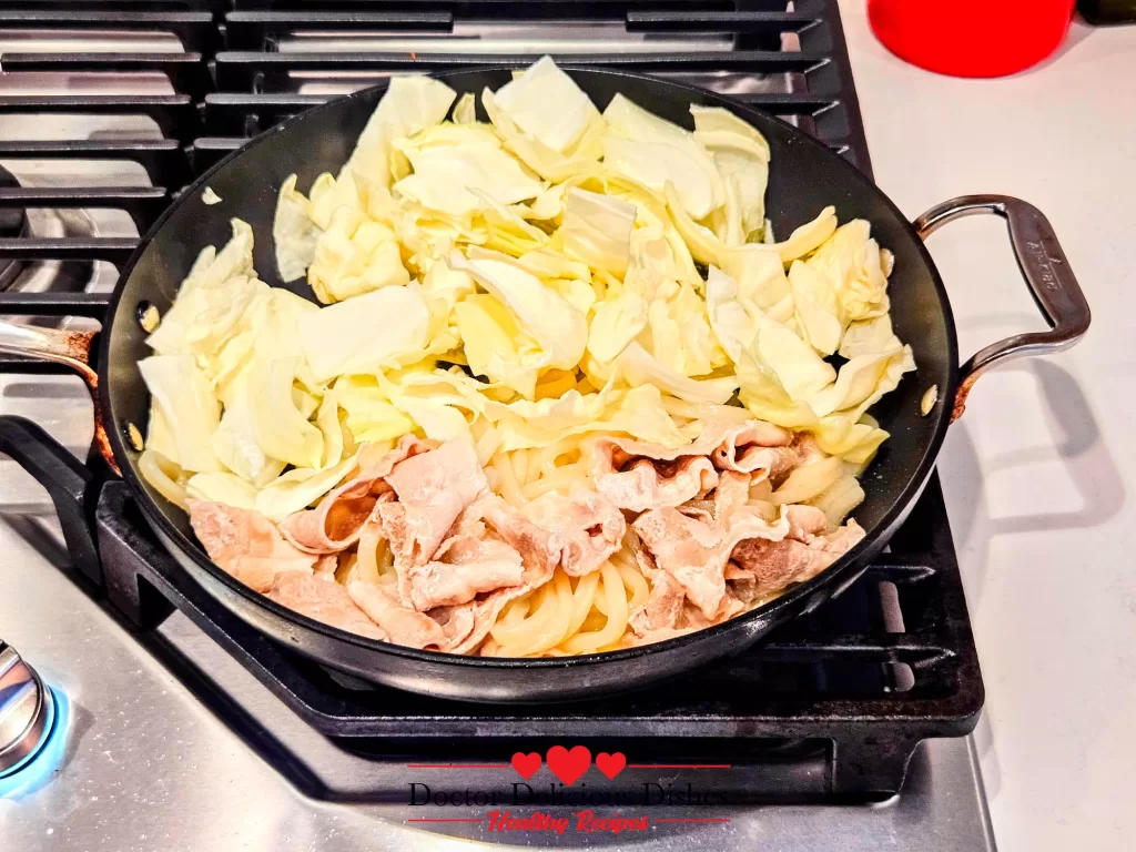 Fresh cabbage added to the skillet with pork and noodles while making Easy Yaki Udon Recipe.