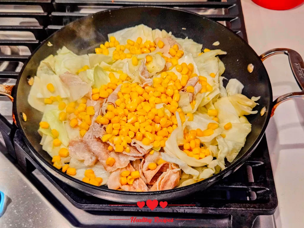 Sweet corn added to the skillet with cabbage and pork while cooking Japanese Yaki Udon Recipe.