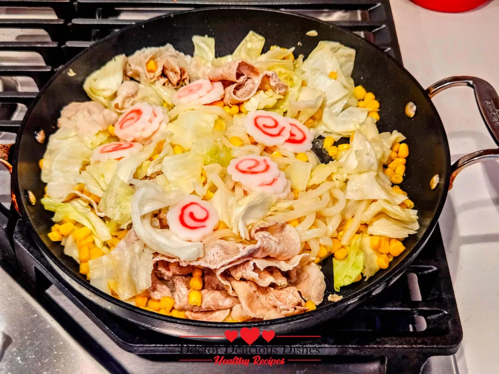Narutomaki fish cakes added to the pan with pork, corn, and cabbage for colorful Easy Yaki Udon Recipe.