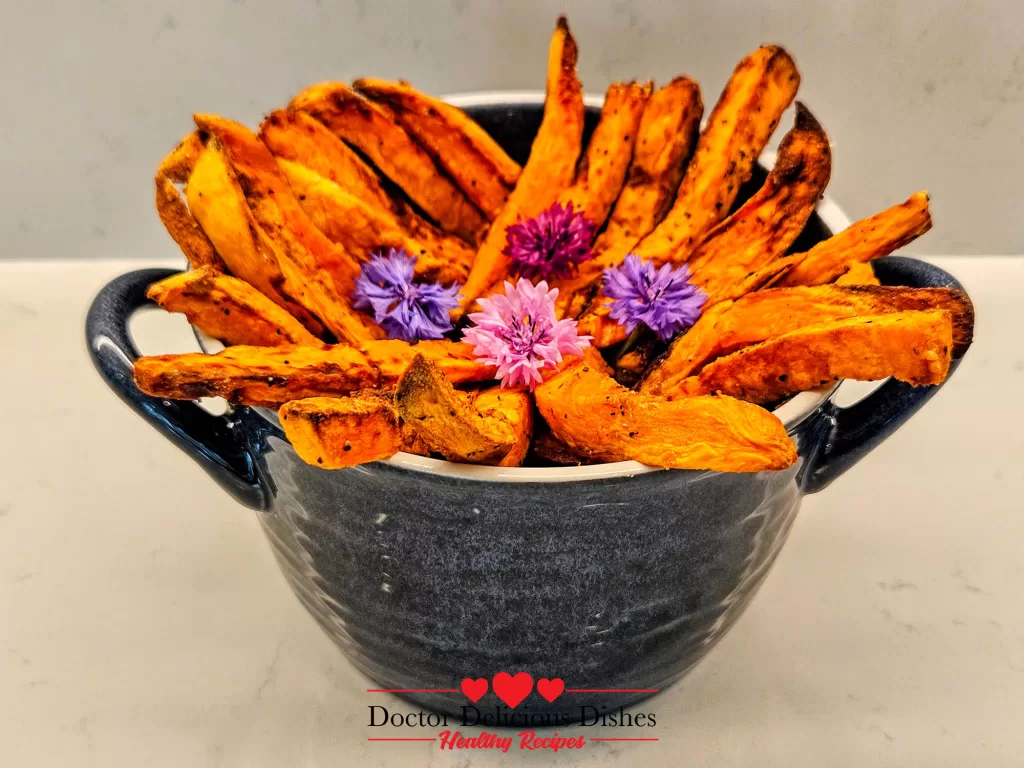 Golden crispy air fryer sweet potato fries styled in a blue bowl with edible flowers – Doctor Delicious Dishes