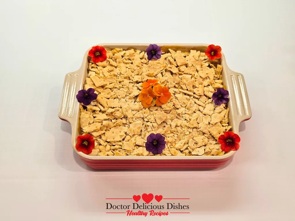 Easy Corn Casserole Recipe topped with crushed crackers and edible flowers in a red baking dish.