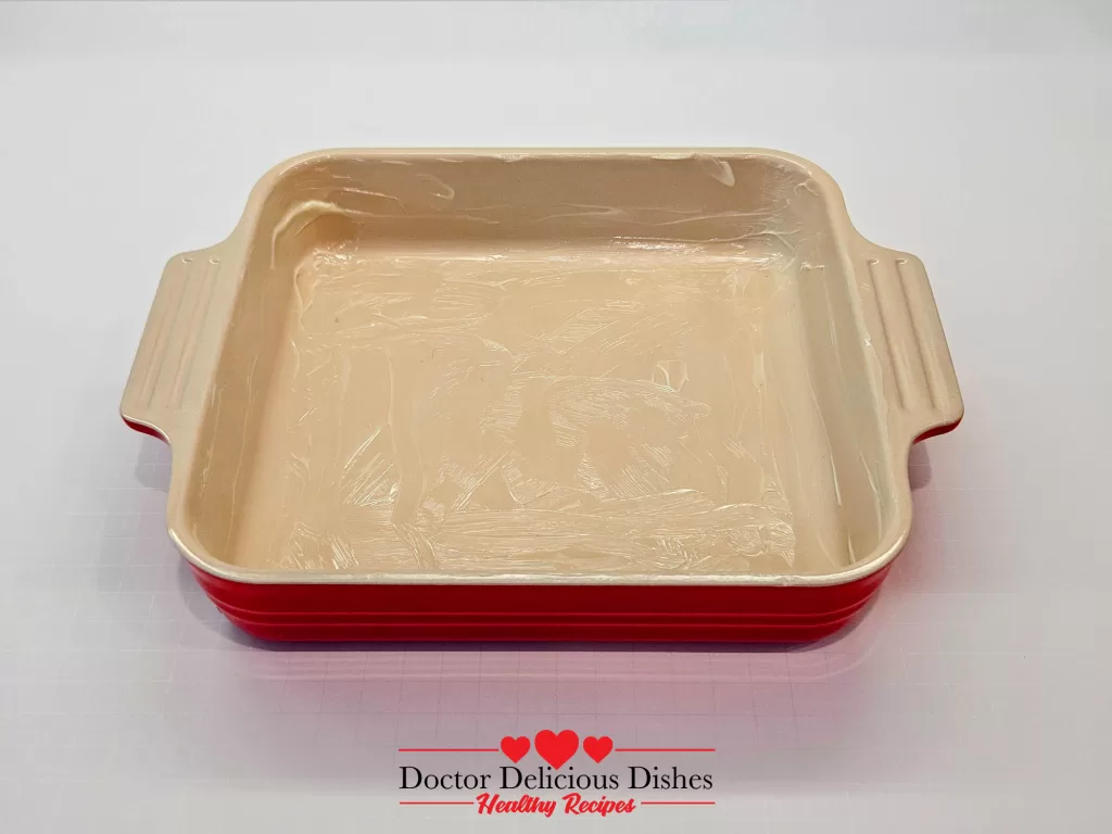 Greased red baking dish ready for the Easy Corn Casserole Recipe preparation.