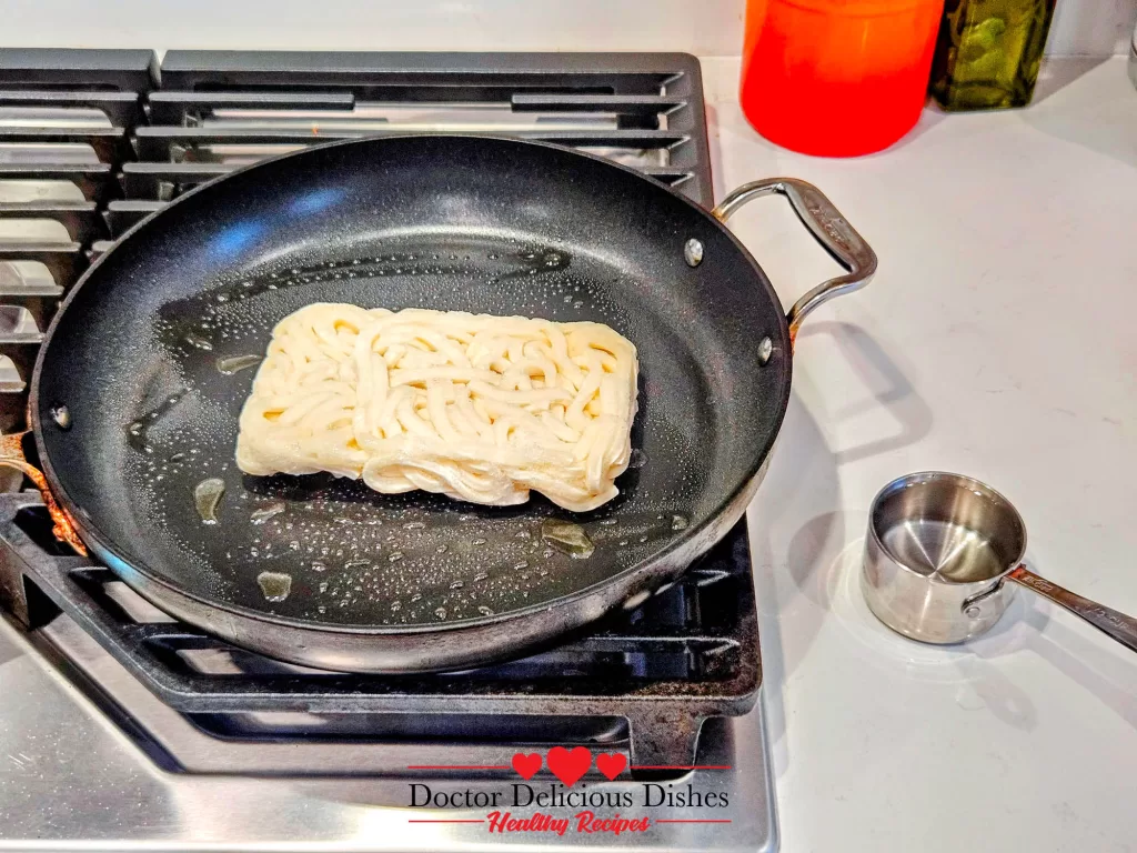Frozen udon noodles placed in a hot pan to begin making Easy Yaki Udon Recipe.