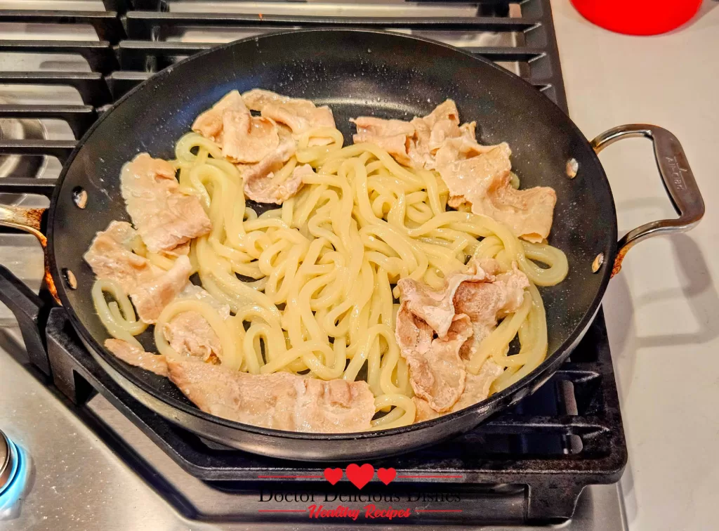 Pork slices cooking together with udon noodles in a hot pan for Easy Yaki Udon Recipe.