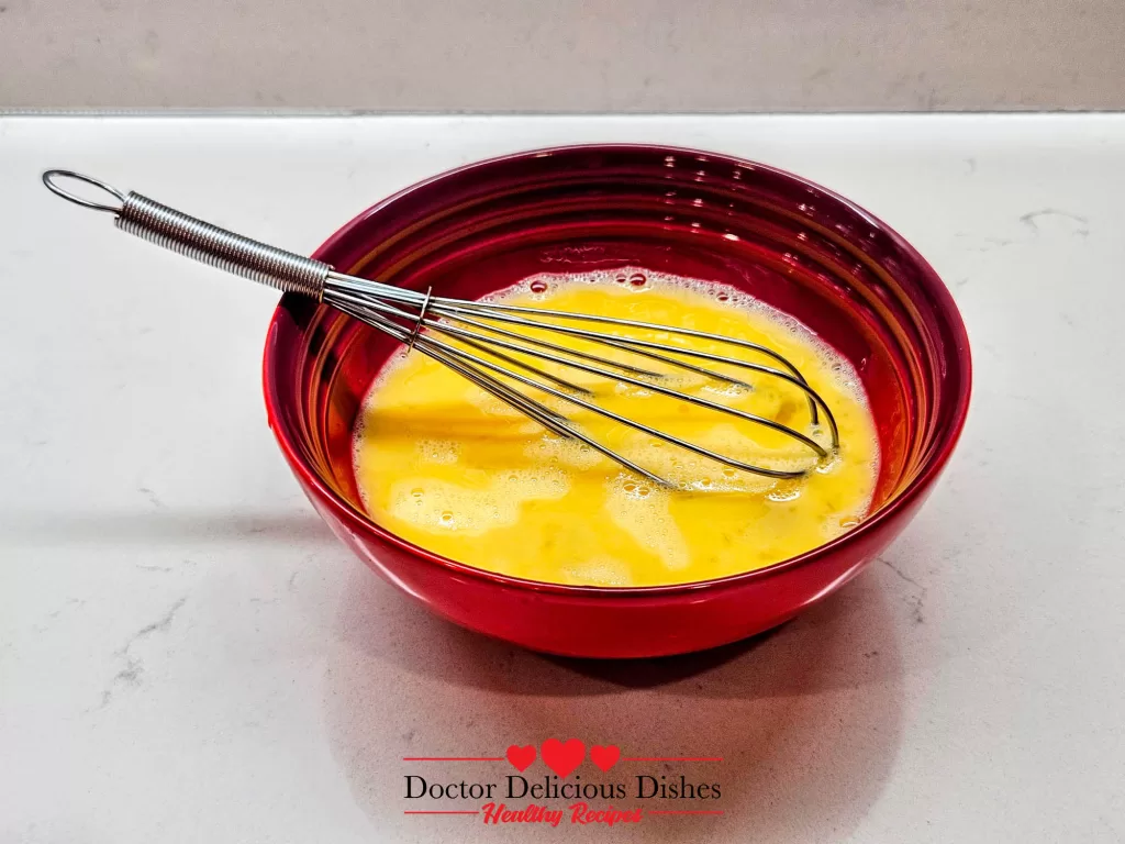 Beaten eggs whisked in a red bowl ready to cook for Chicken Soboro Don by Doctor Delicious Dishes.