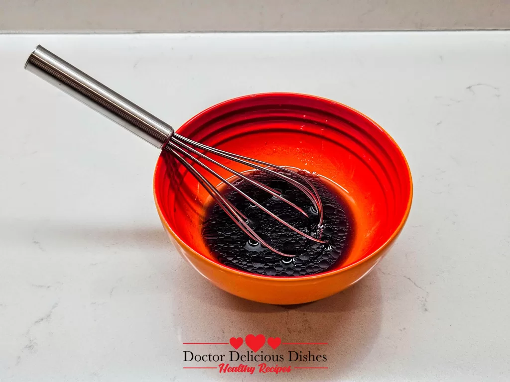 Sweet and savory soy-based sauce mixture for Chicken Soboro Don being whisked in an orange bowl by Doctor Delicious Dishes.